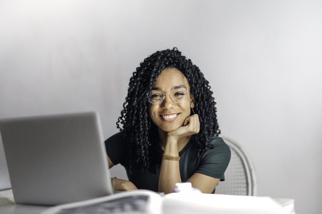 joyful businesswoman with curly hair smiling at camera while using laptop indoors. 3769021
